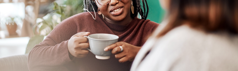 Woman holding coffee cup while talking to friend 